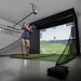 Person practicing golf swings in a home indoor simulator setup.