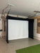 Indoor golf simulator setup with a Vanish Lite screen and ceiling mount in a garage.