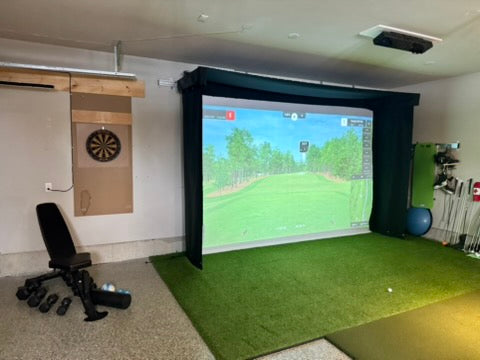 Indoor golf simulator setup with Vanish Lite screen displaying a golf course, surrounded by golf equipment and a dartboard.