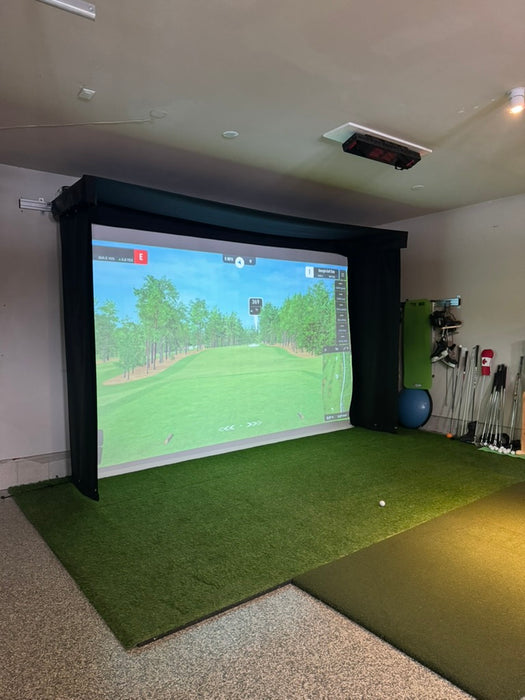 Indoor golf simulator setup with Vanish Lite screen displaying a golf course and grass mat on the floor.