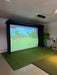 Indoor golf simulator setup with Vanish Lite screen displaying a golf course and grass mat on the floor.